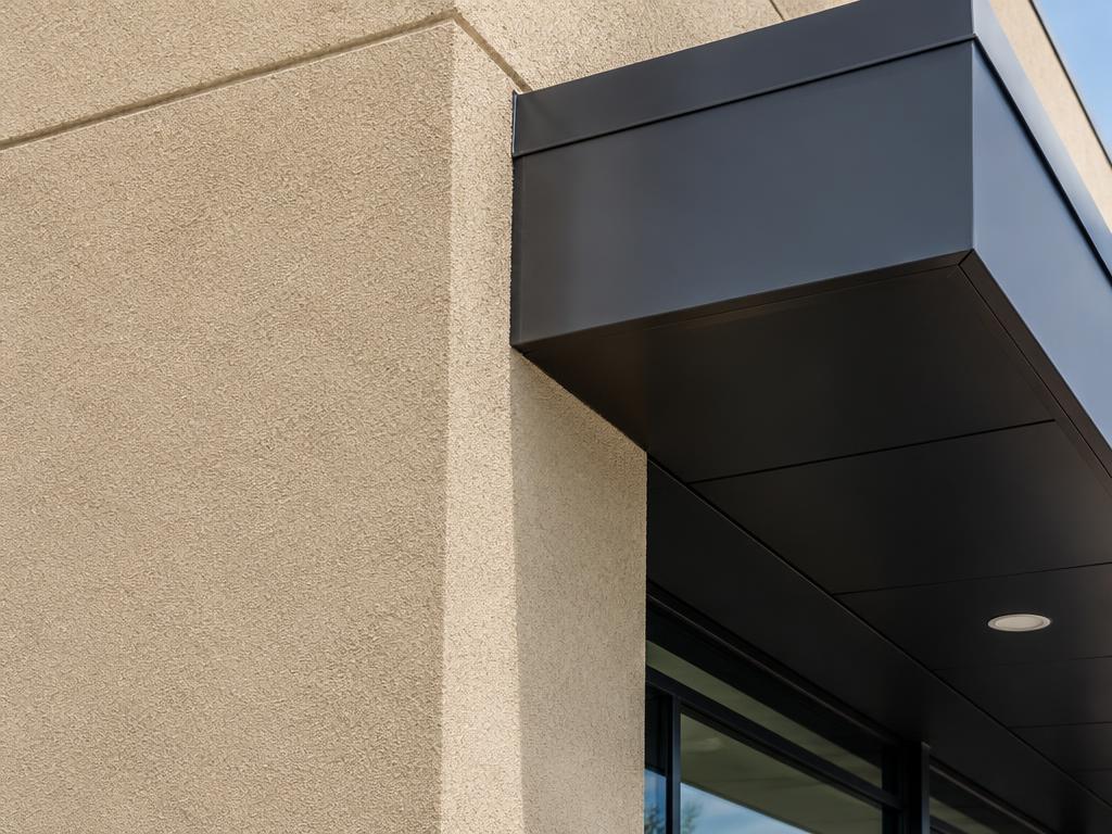 Sand stucco storefront corner meeting a charcoal metal canopy
