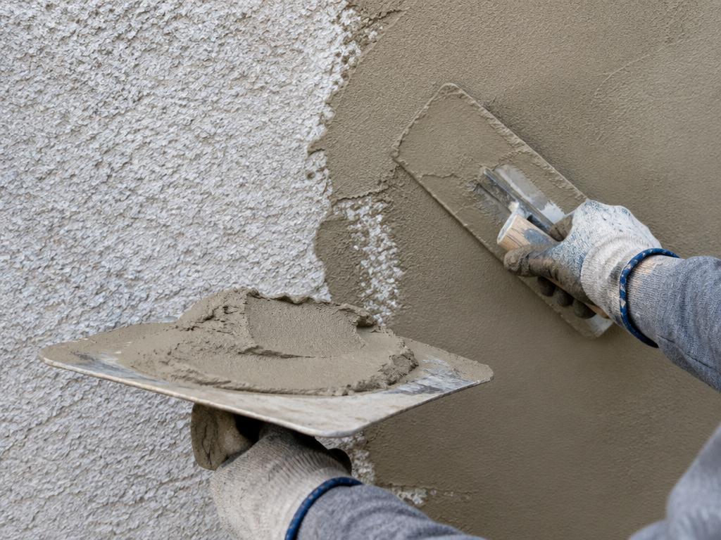 Hawk and trowel applying a greige color coat over existing stucco